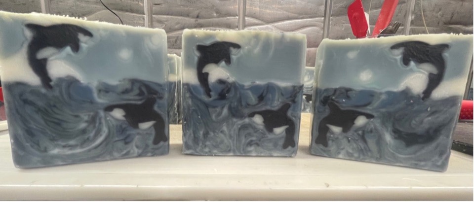 Three Breach for It bars, each with two black-and-white orcas leaping from blue-grey swirled waves, on a white counter