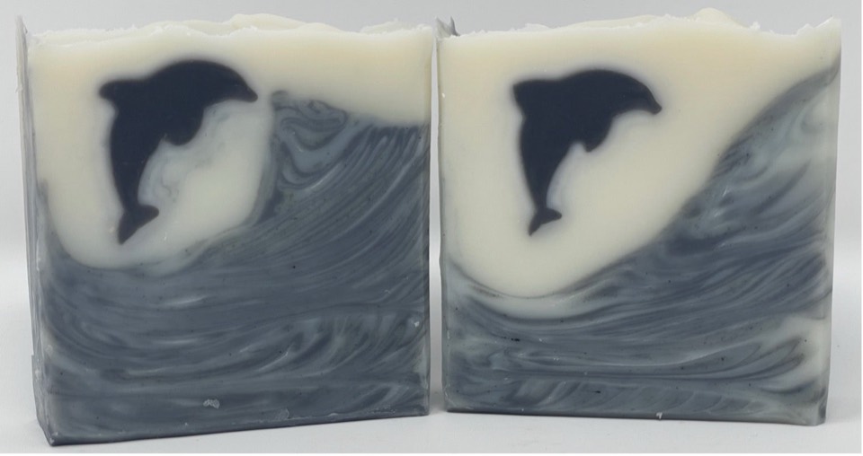 Two Ebb & Flow Porpoise bars with black porpoise shapes on cream above swirling grey-blue waves, on white