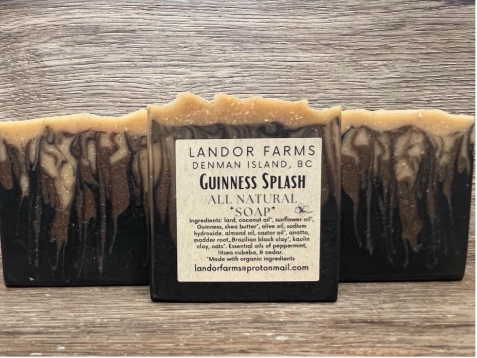Three Guinness Splash soap bars, black with brown and tan drip swirls, the middle one with a Landor Farms label, on wood