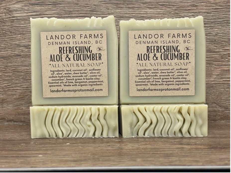 Four Refreshing Aloe & Cucumber bars on wood: two with Landor Farms labels, each standing on a pale green bar with a wavy top