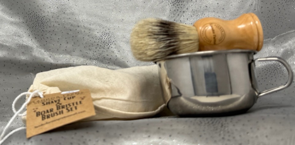 Shave Cup & Brush Set: wooden-handled boar bristle brush in a stainless-steel mug beside a muslin bag with a kraft tag