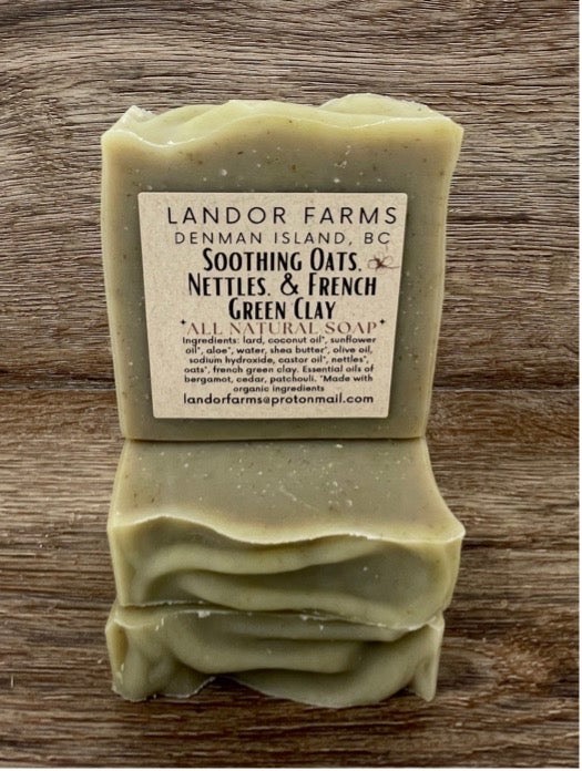 Three stacked sage-green Soothing Oats & Nettles bars, the top one with a Landor Farms label, on wood