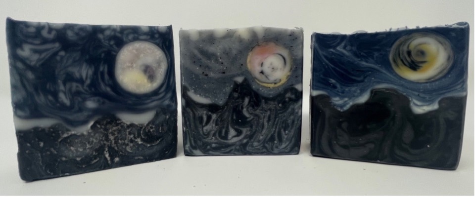 Stormy Skies soap: three bars with swirled dark blue and grey skies, round moons and black mountains, on white